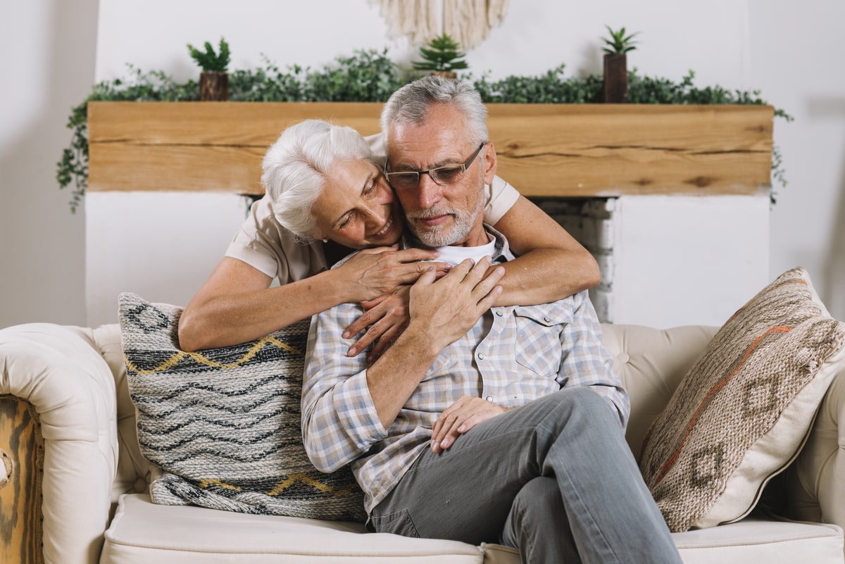 Pareja de personas mayores sonriendo en el salón de su casa.